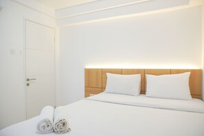 A hotel room with a neatly made bed, a wooden headboard, and a door with a handle. - Good Choice And Minimalist 1Br Bassura City Apartment (Jakarta)