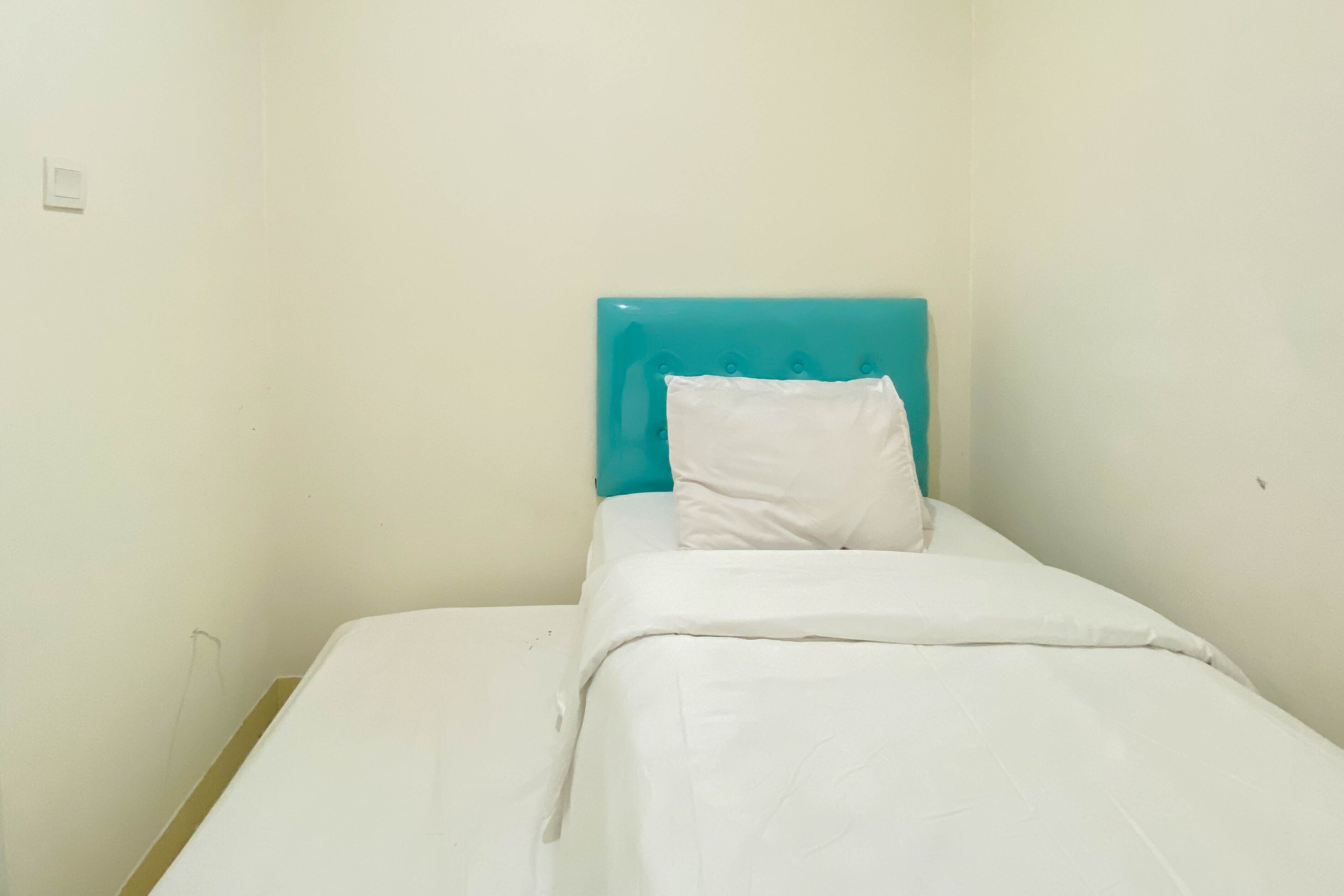 Een kleine kamer met een enkel bed, een blauwgroen hoofdeinde en witte beddengoed.