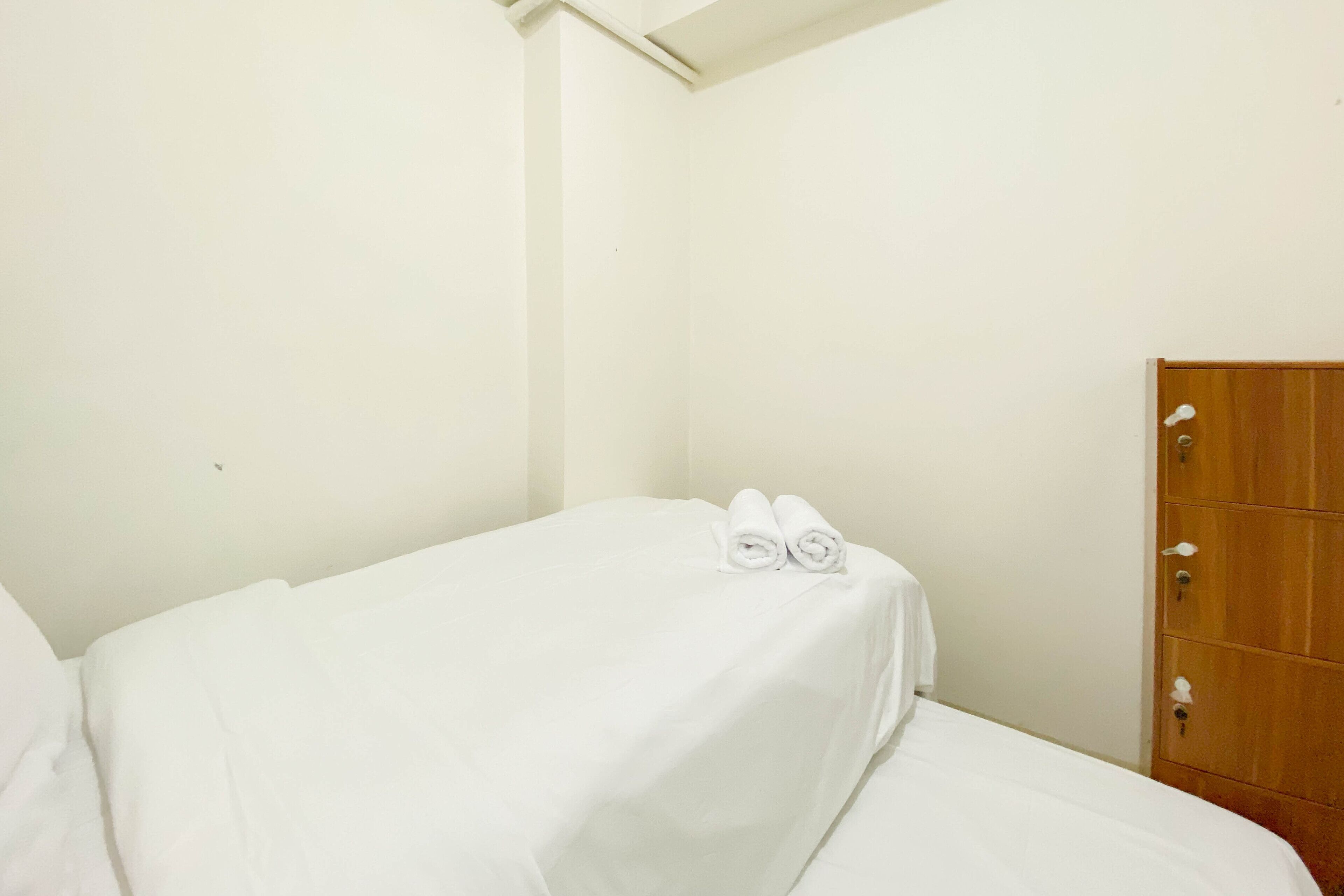 A single bed with white bedding and two rolled towels on top.