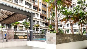 A multi-story residential building with balconies, a covered walkway, and a swimming pool area. - Comfy and Modern Look 1BR LRT City Jatibening Apartment (Bekasi)