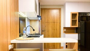 A compact kitchen with a white countertop, wooden cabinets, a black refrigerator, and two wooden stools. - Comfy and Modern Look 1BR LRT City Jatibening Apartment (Bekasi)
