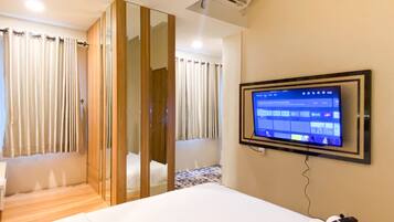Habitación de hotel con cama, televisor montado en la pared, armario de madera y baño con cortina de ducha.