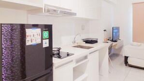 Cozinha moderna com frigorífico, pia e fogão. Existe um pequeno espaço de refeições com uma cadeira e uma televisão.