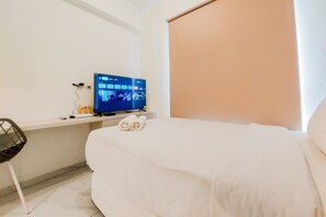A hotel room with a bed, a desk with a computer, and a window with a blind. - Stunning And Strategic Studio Apartment Sky House Alam Sutera (Tangerang)