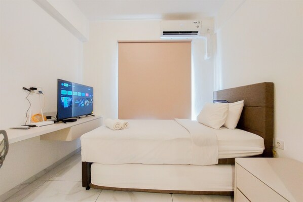 A hotel room with a bed, a TV, a desk, and an air conditioning unit. - Stunning And Strategic Studio Apartment Sky House Alam Sutera (Tangerang)