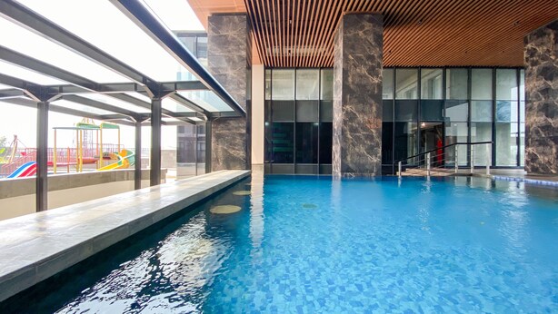 An indoor swimming pool with clear water, surrounded by glass walls and a wooden ceiling. - Good Choice Studio Apartment Anwa Residence Bintaro (South Tangerang)