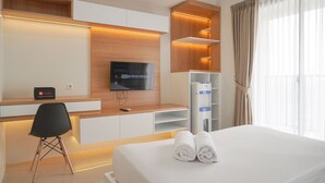 A modern hotel room with a bed, a desk with a chair, a flat-screen TV, and a minibar. - Good Choice Studio Apartment Anwa Residence Bintaro (South Tangerang)