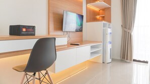 A modern hotel room with a wooden accent wall, a flat-screen TV, a minibar, and a seating area with a chair. - Good Choice Studio Apartment Anwa Residence Bintaro (South Tangerang)