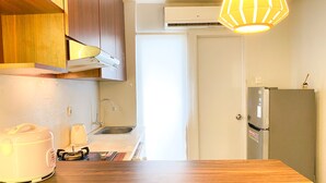 Ett kompakt kök med träskåp, en diskho i rostfritt stål, ett vitt kylskåp och en hängande lampa.
