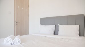 Een net opgemaakt bed met witte lakens en kussens, een grijze hoofdbord en een houten deur met een handvat.