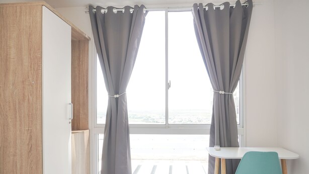 Een kamer met een groot raam, een witte tafel, een blauwgroene stoel en een houten garderobe.