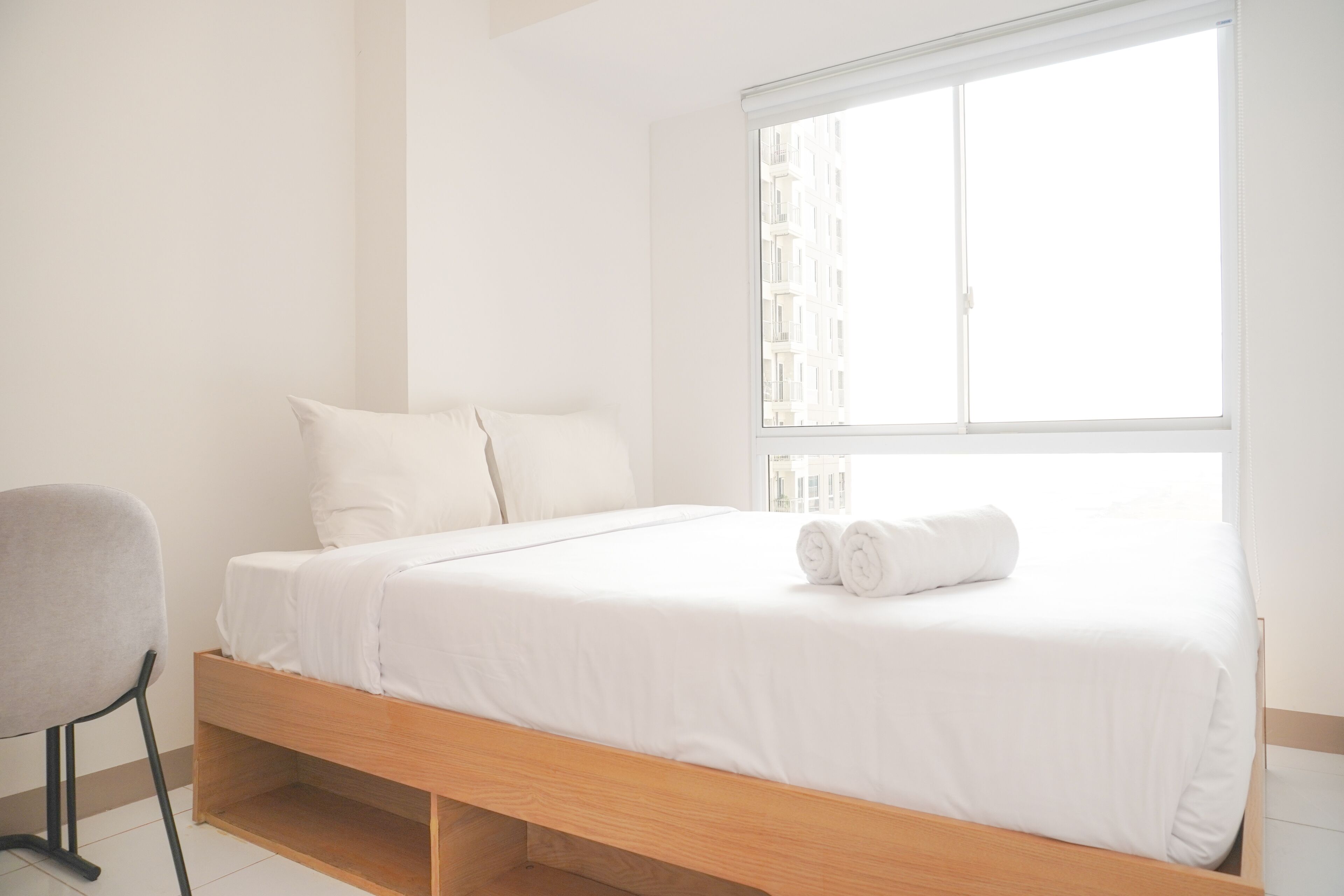 Quarto de hotel minimalista com uma cama de solteiro, uma cadeira e uma janela grande.