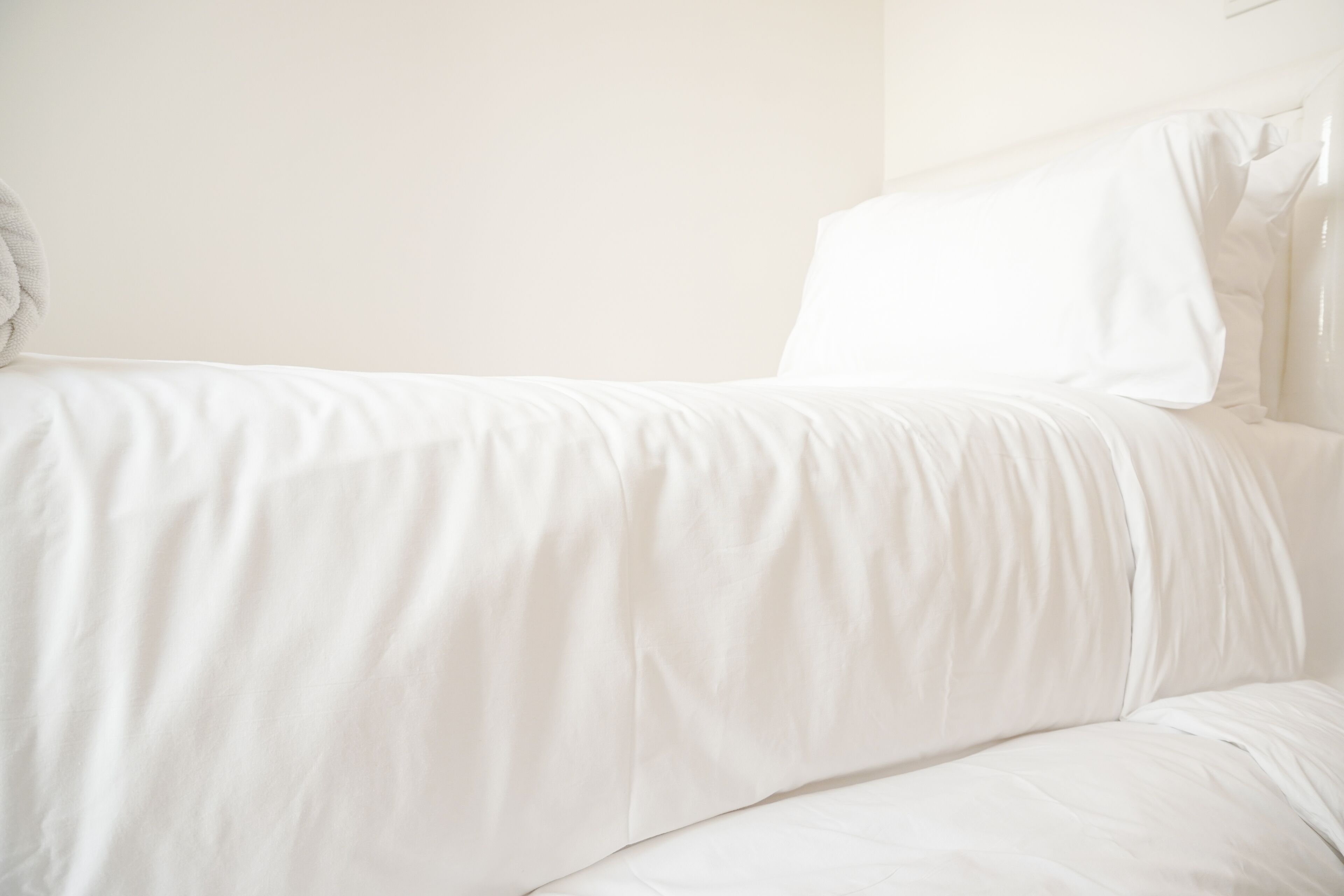 A white bed with a pillow and a blanket.