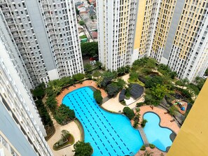 Un edificio residencial alto con una gran piscina rodeada de vegetación y una zona de juegos infantil.