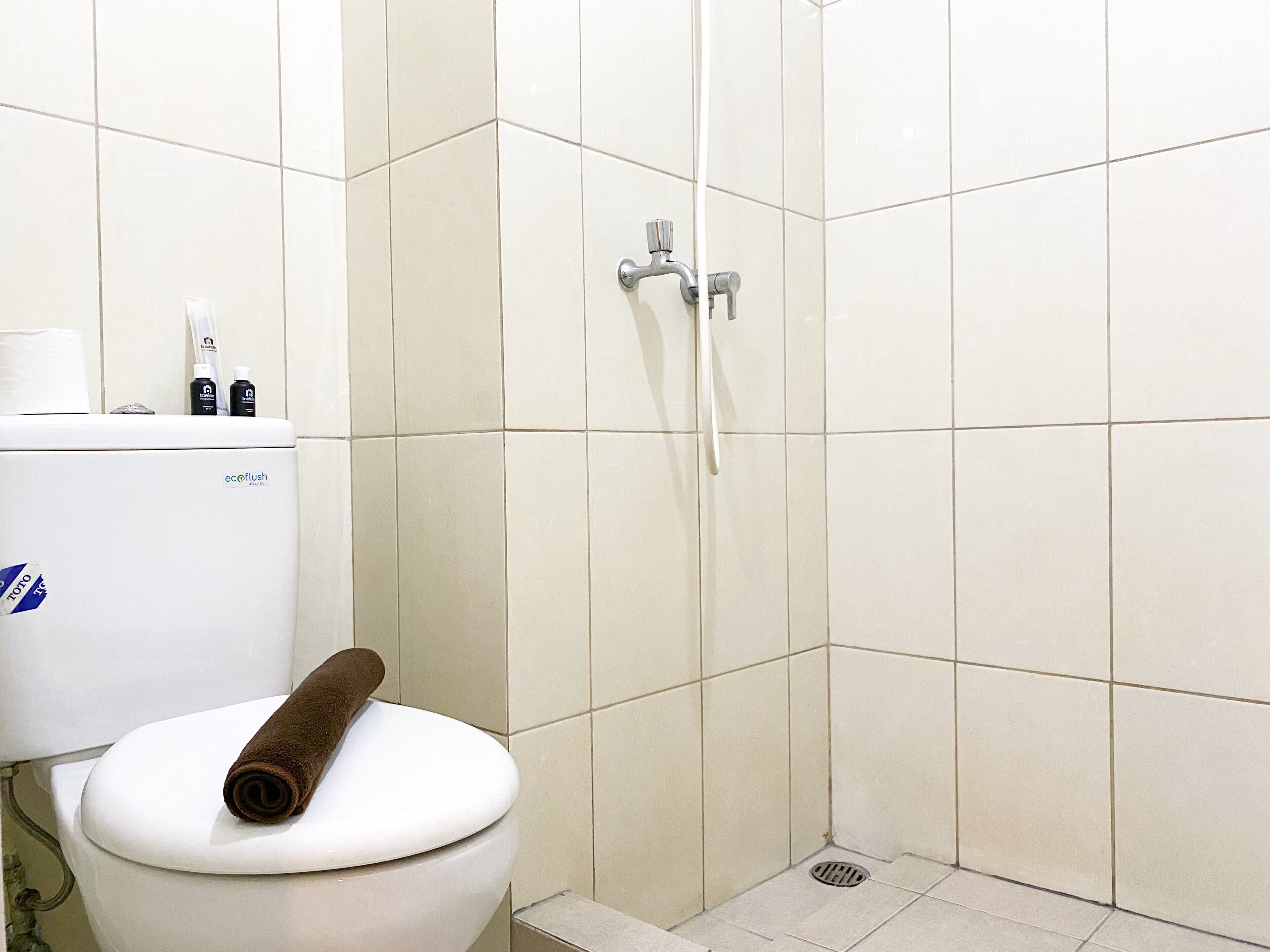 A bathroom with a toilet, a shower, and a toilet paper holder with toiletries.