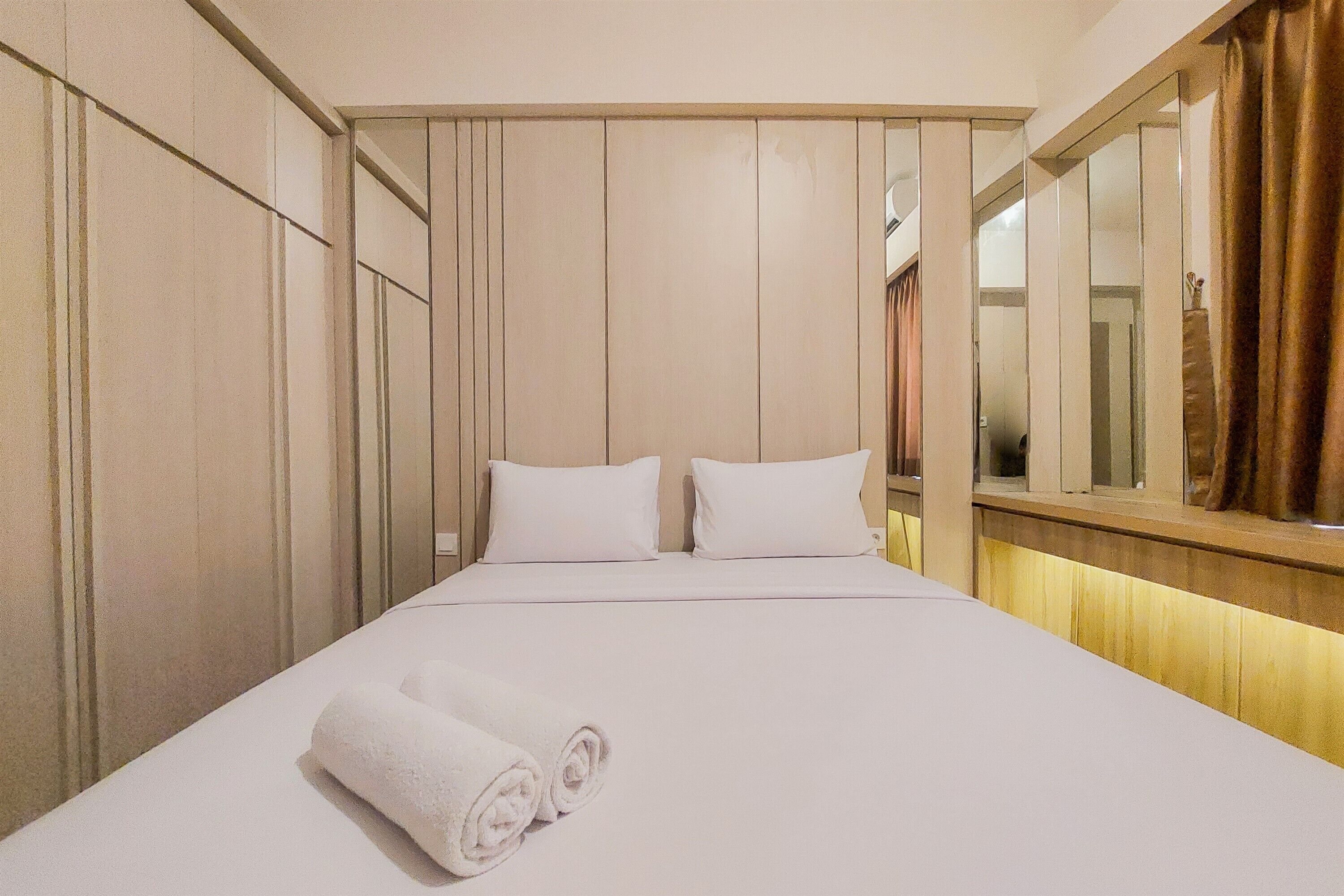 A hotel room with a large bed, two pillows, a rolled white towel, and a mirror on the wall.