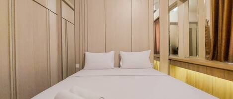 A hotel room with a large bed, two pillows, a rolled white towel, and a mirror on the wall.