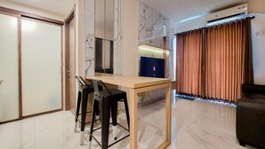 Una sala de estar moderna con una mesa de madera, dos sillas negras, un televisor y un ventanal con cortinas.