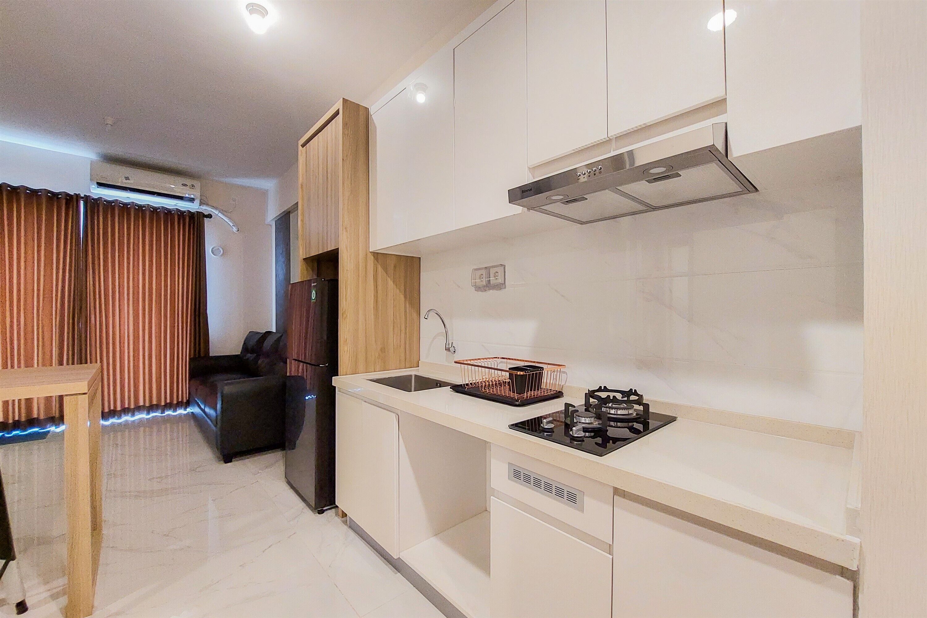 A modern kitchen with a built-in stove, sink, and ventilation hood. There is a wooden cabinet and a black chair in the adjacent living area.