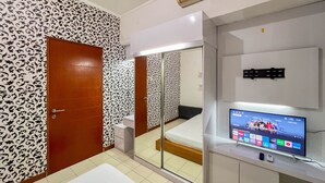 A hotel room with a large mirror, a wooden door, a bed, a TV, and a small table. - Cozy 1Br At Marbella Suites Dago Pakar Bandung Apartment (Bandung)