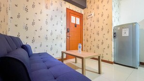 A room with a blue sofa, a wooden table with a water bottle, a refrigerator, and a door with a lock and a notice. - Cozy 1Br At Marbella Suites Dago Pakar Bandung Apartment (Bandung)