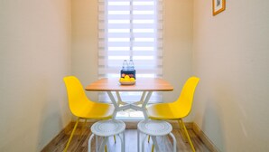 A dining area with a wooden table, two yellow chairs, and a small white table with a bowl of lemons and a box of lemons. - Spacious 2Br Combined Tokyo Riverside Pik 2 Apartment (Teluknaga)