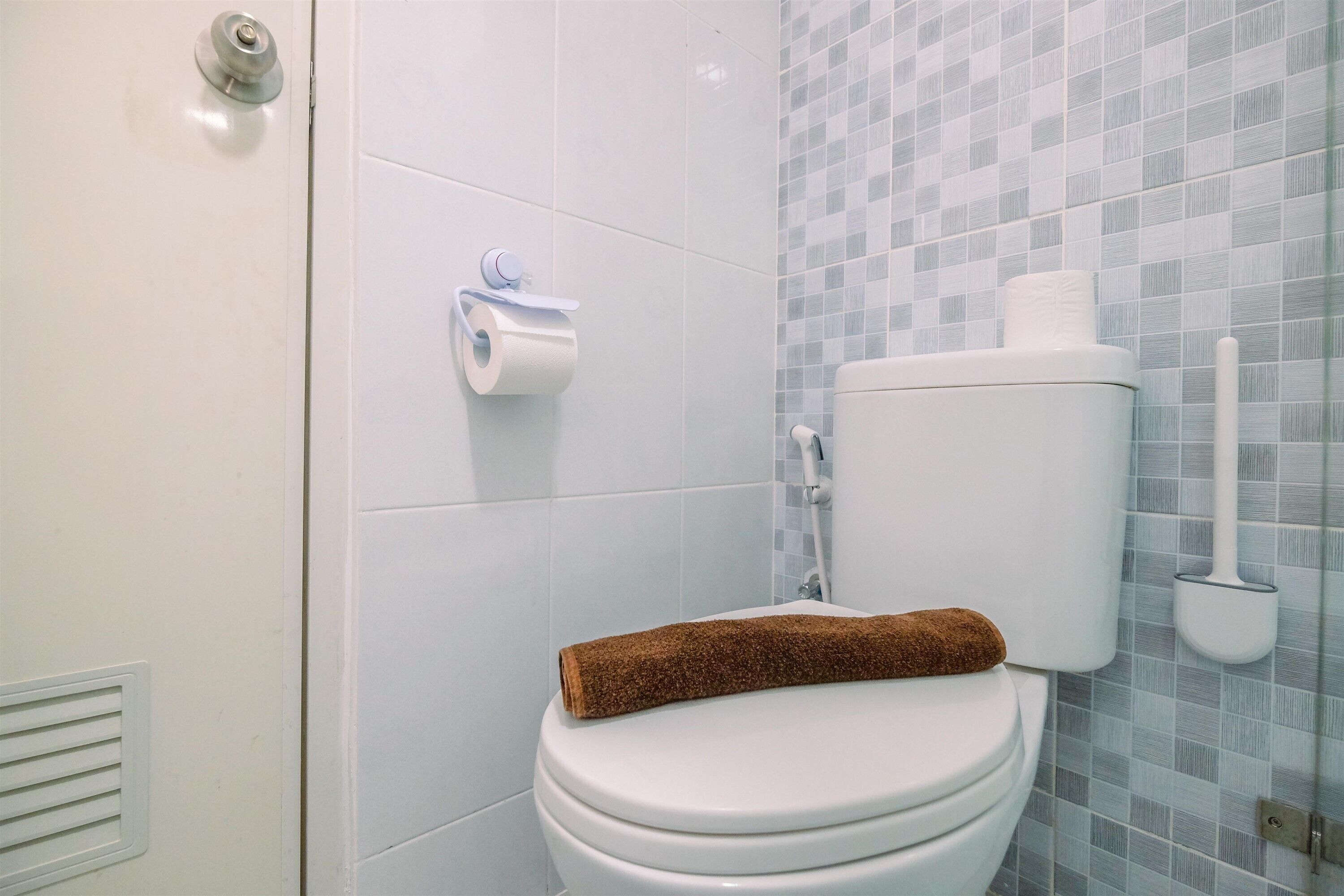 A bathroom with a toilet, a towel, and a toilet paper holder.