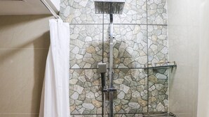 A shower with a stone wall backdrop, a glass shelf, and a white shower curtain. - Spacious Studio The Edge Bandung Apartment (Cimahi)