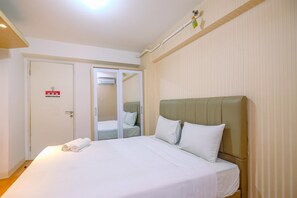 A hotel room with a large bed, a door with a fire alarm, and a mirror. - Best Deal And Simply Studio Bassura City Apartment (Jakarta)