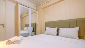 Ein Hotelzimmer mit Bett, weißen Laken, einem grünen Kopfteil und einem Holzschrank mit Spiegel.
