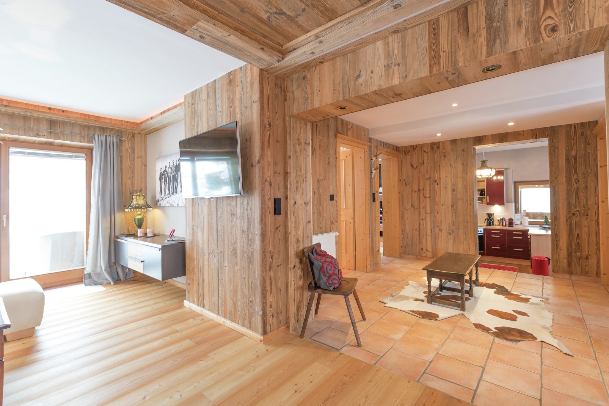 Une pièce aux murs en bois, dotée d’un téléviseur à écran plat, d’un bureau, d’une chaise, d’une table et d’un tapis en peau de vache.