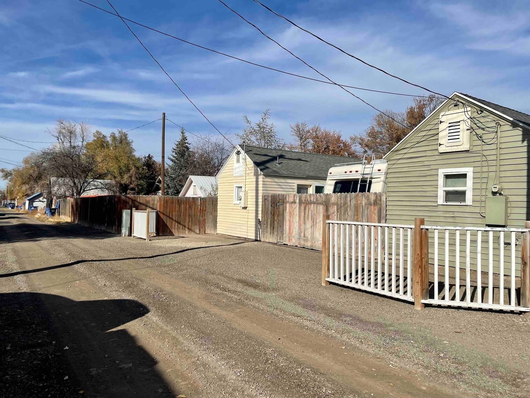A rural road with a dirt path, wooden fences, and a trailer.