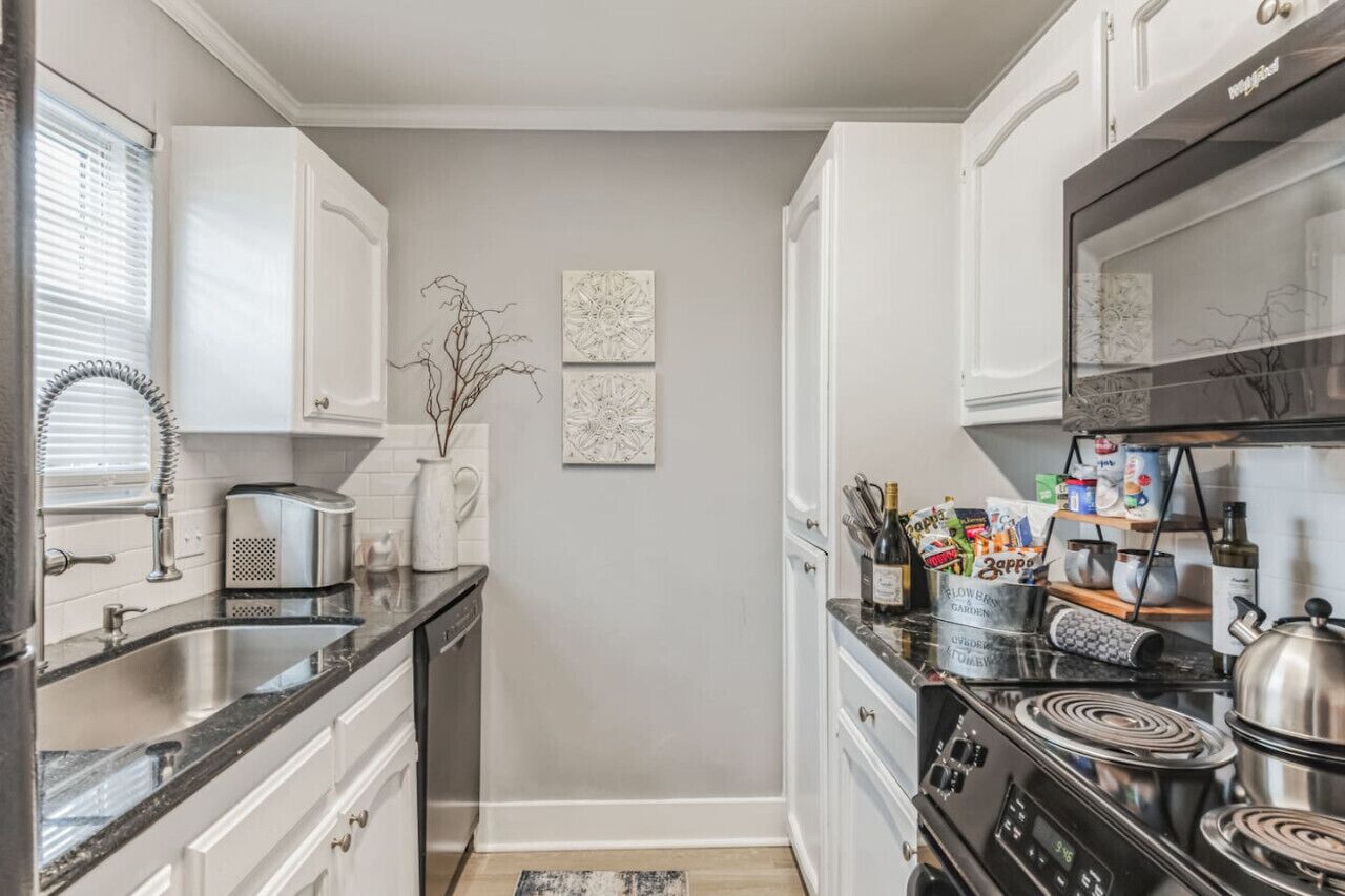 A kitchen with white cabinets, a black stove, and a window with blinds.