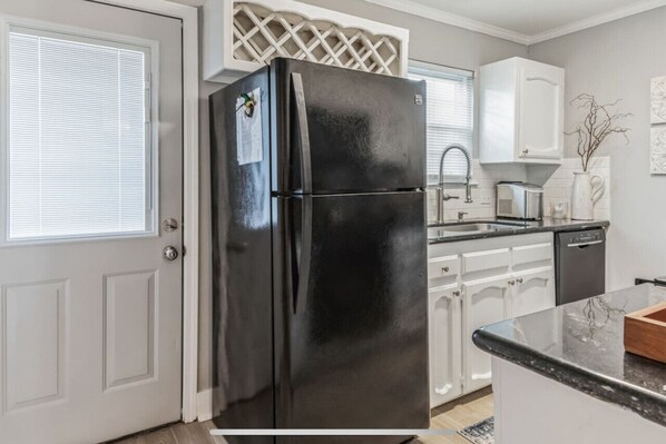 A kitchen with a black refrigerator, white cabinets, a sink, and a dishwasher. - Charming two ensuites near hospitals & shops. Jefferson Hwy•Bluebonnet (Baton Rouge)