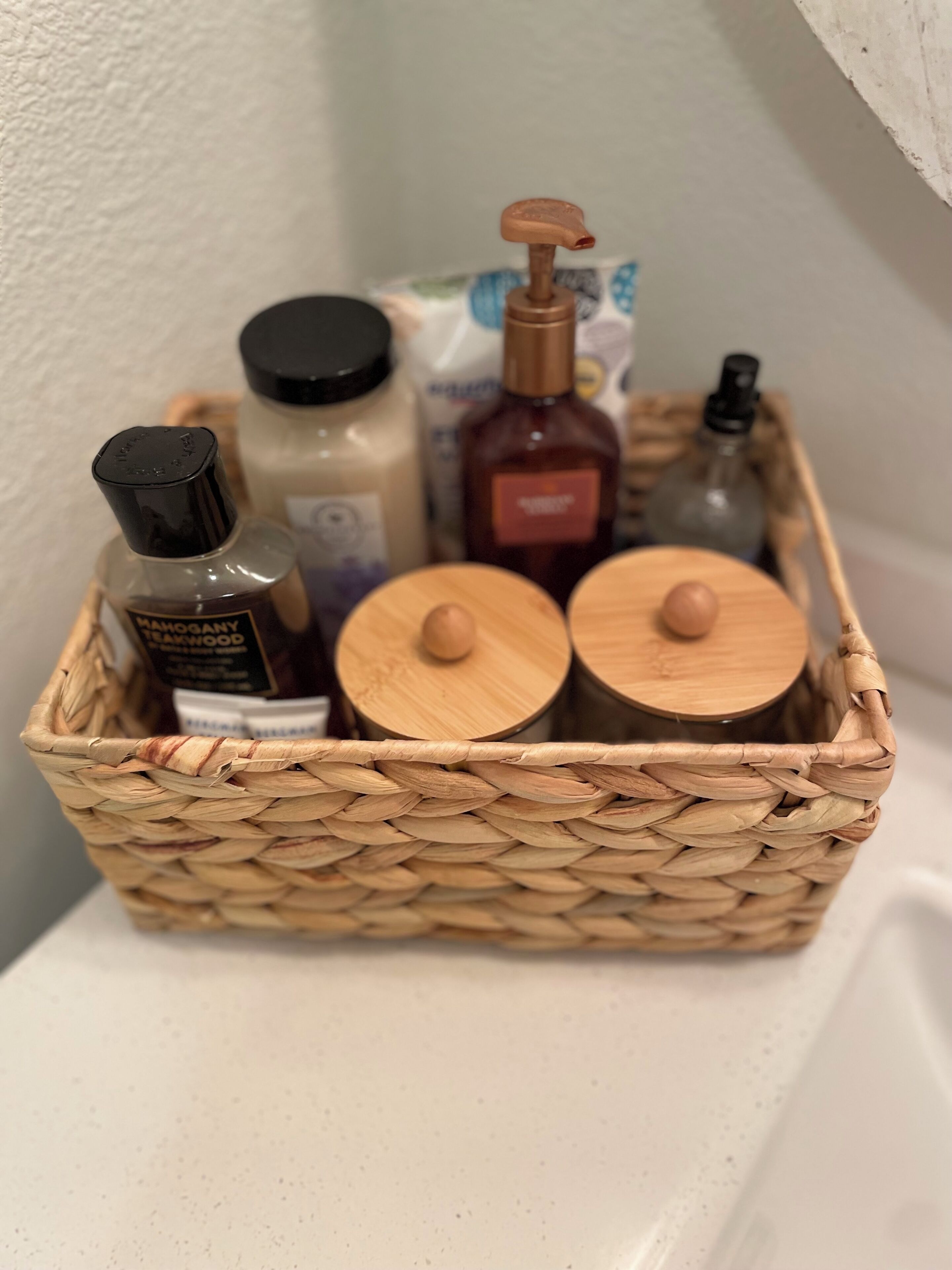 A wicker basket containing various toiletries and two wooden containers with lids.