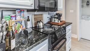 A kitchen with white cabinets, a black microwave, a coffee maker, and a stove. - Charming two ensuites near hospitals & shops. Jefferson Hwy•Bluebonnet (Baton Rouge)