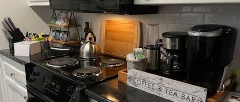 A kitchen with a coffee and tea bar, a kettle, a coffee maker, and various kitchen utensils.
