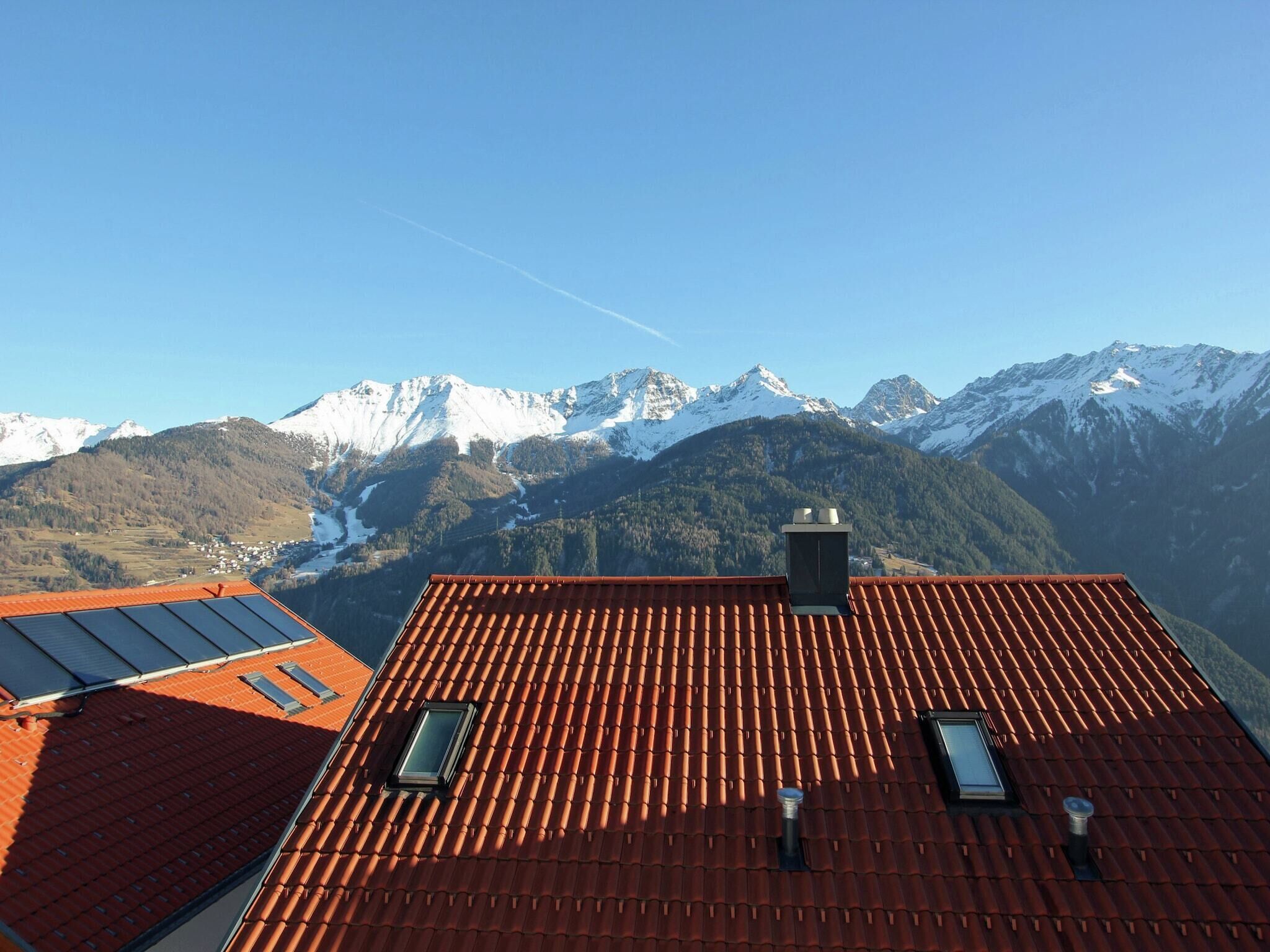 A building with a red-tiled roof, two skylights, and a view of snow-capped mountains.