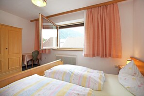 Una camera da letto con due letti, un armadio in legno, una sedia, una finestra con tende e un termosifone.