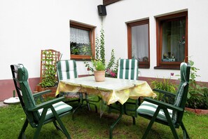 Un piccolo patio esterno con un tavolo e quattro sedie, circondato da un muro bianco con finestre e un recinto in legno.