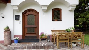 Un edificio blanco con puerta de madera, una banca, una mesa y plantas en macetas.