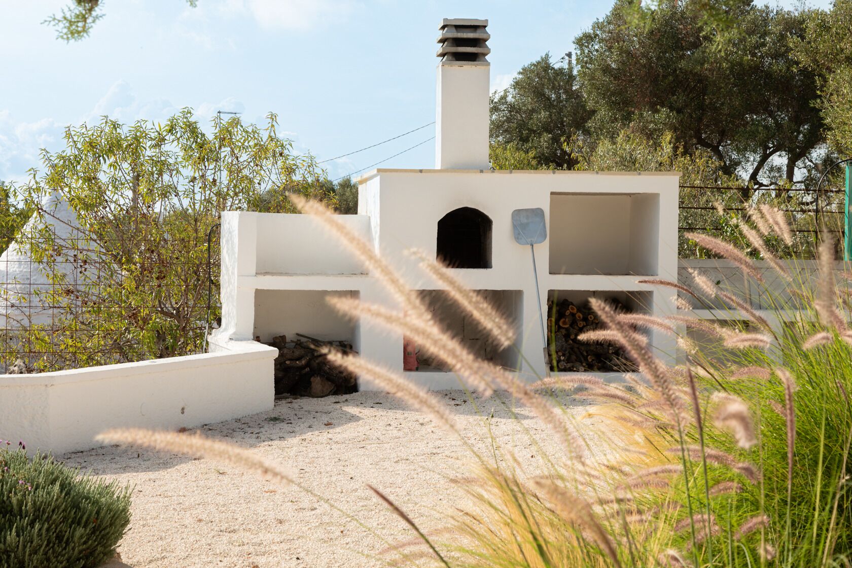 A modern outdoor structure with a chimney, a small enclosed area with a bench, and a gravel path.