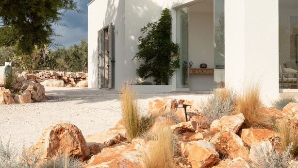 Une maison moderne dotée de grandes baies vitrées, d’un mur en pierre et d’un jardin de style désertique agrémenté de rochers et de cactus.