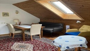 A cozy room with a sloped ceiling, a dining table with chairs, a sofa, and a small table with a tablecloth. - Apartment in Eberndorf near Petzen Ski Area (Eberndorf)