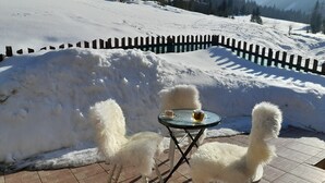 A snow-covered outdoor seating area with a table and chairs, surrounded by a wooden fence and snowbanks.