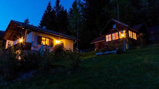 Two cabins with visible windows and a wooden exterior, surrounded by trees and a grassy area.