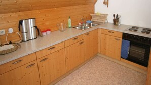 A compact kitchen with wooden cabinets, a sink, a stove, and a coffee maker.