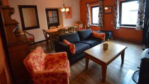 A cozy living room with a sofa, floral armchair, wooden coffee table, and a dining area with a table and chairs.