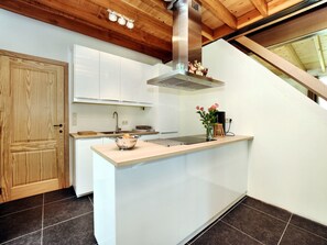 A modern kitchen with white cabinets, a stainless steel range hood, and a wooden ceiling.