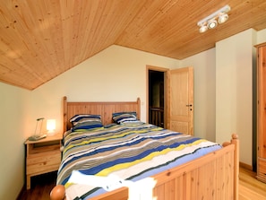 Een slaapkamer met een houten plafond, een bed met gestreept beddengoed, een nachtkastje met een lamp en een kledingkast.